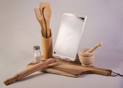 A closeup shot of  wooden kitchenware and a tablet on a gray background