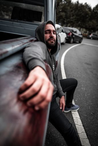 A portrait of a Hispanic man leaning against the side of a pick-up truck on the road