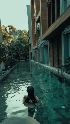 A woman in a swimsuit enjoys a luxurious hotel pool surrounded by modern architecture and lush greenery.