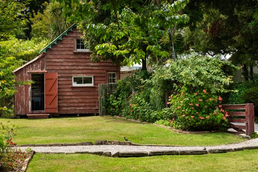 Rustic wooden shed with open door surrounded by greenery and flowers