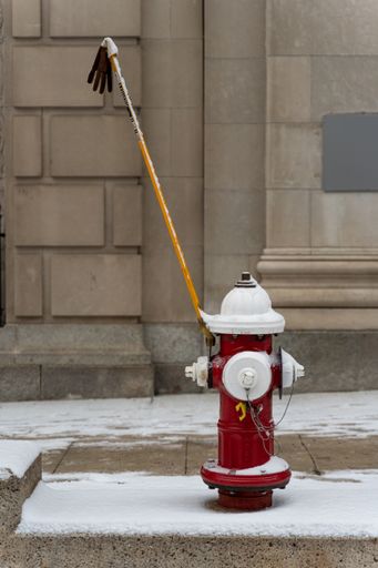 A vertical closeup shot of a stick with a glove attached to a red hydrant on the side of the road