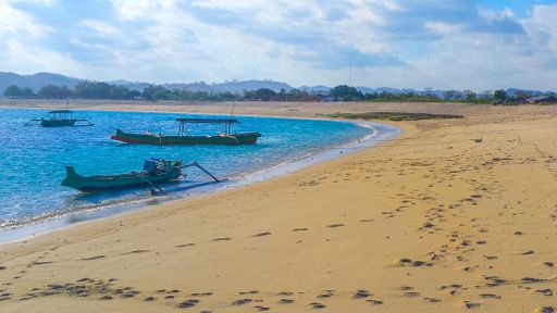 Beautiful paradise lagoon beach background with white sand, blue water and clear sky and a small longtail boats at Tanjung An on Lombok in Indonesia.