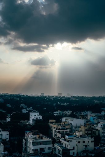 Dramatic urban skyline with sun rays breaking through dark clouds over a cityscape, creating a striking contrast.