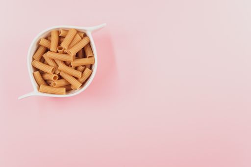 A high angle shot of a bowl of uncooked pasta on a pink surface