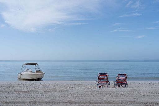 Serene beach scene with two empty chairs and a boat on a calm sea under a clear blue sky, perfect for relaxation and vacations.