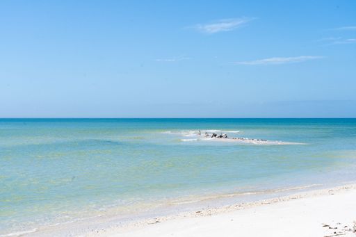 A serene beach scene with clear turquoise waters and a bright blue sky, featuring a sandy shoreline.