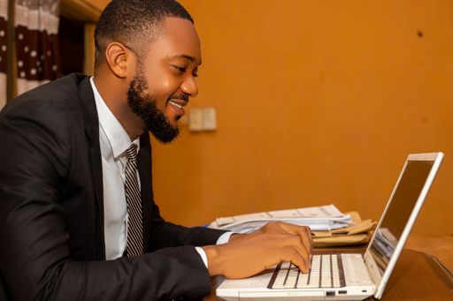A smiling African businessman in a black suit working with his laptop