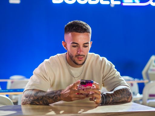 A portrait of an attractive Spanish man with tattoos texting on his phone in a bowling arena