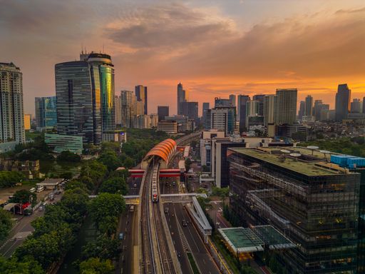 Aerial view of Jakarta cityscape at sunset with skyscrapers and a train on the track, showcasing urban development and vibrant skies.