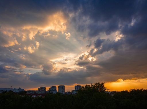 Dramatic sunset over a city skyline with vibrant clouds and golden hues, capturing the transition from day to night.