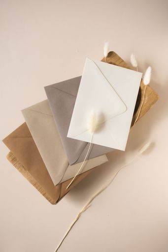 Minimalist arrangement of neutral-toned envelopes with dried flowers on a beige background, creating an elegant and serene atmosphere.