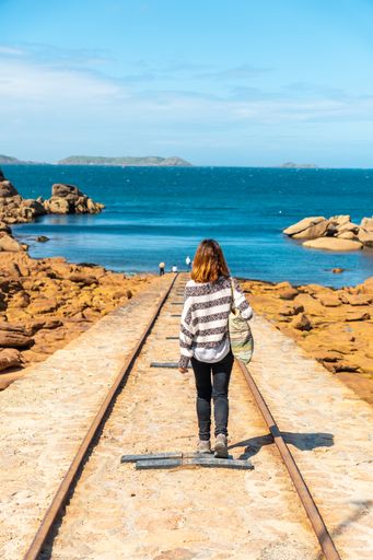 A vertical shot of a female standing on a path at the sea along Lighthouse Mean Ruz, Britany