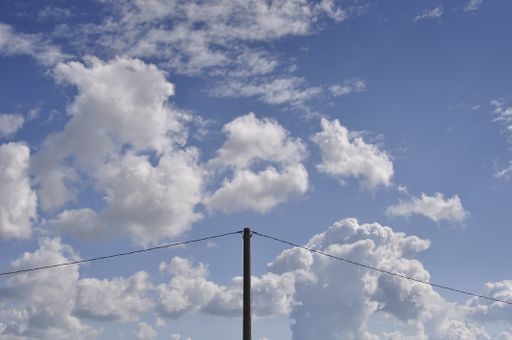 A beautiful shot of white clouds in the blue sky with an electricity pole in the middle
