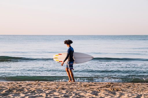 A young Afro Latino with a surfboard in the sea