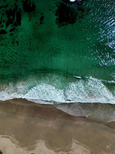 Aerial view of a pristine beach with emerald green waves crashing on the sandy shore, showcasing nature's beauty from above.
