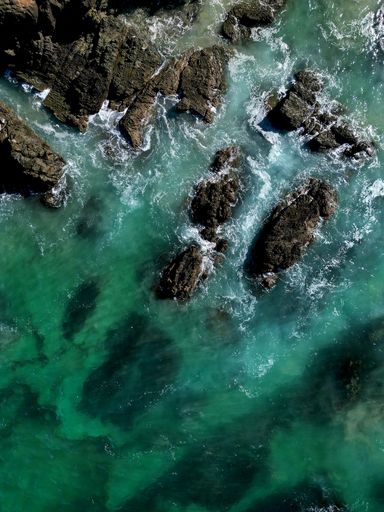 Aerial view of turquoise ocean waves crashing against rocky coastline, creating a stunning natural pattern.
