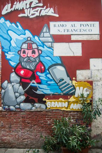 A vertical shot of colorful graffiti on the brick wall with a green plant in the foreground in Venice