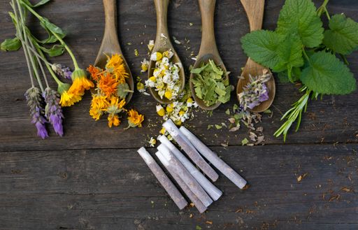 Assorted dried herbs and flowers with wooden spoons on rustic wooden background, showcasing natural ingredients for herbal remedies.