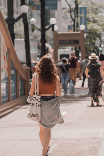 A vertical shot of a young stylish female from the back walking on the paved road