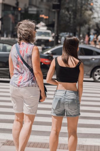 A vertical shot of a middle-aged woman and a young stylish female from the back crossing the street