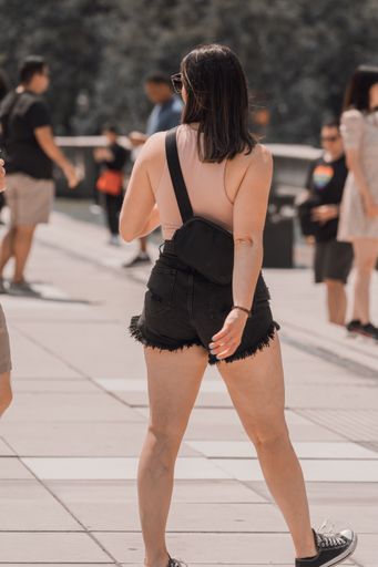 A vertical shot of a young stylish female from the back walking on the paved road