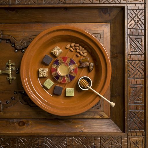 An overhead shot of a round wooden plate with different kinds of square-shaped sweets and nuts with honey