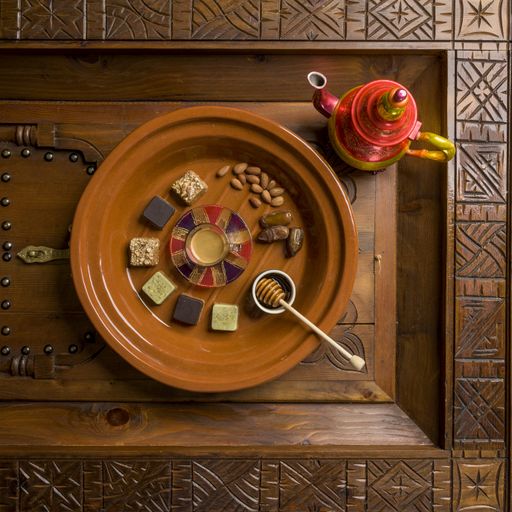 An overhead shot of a round wooden plate with different kinds of square-shaped sweets and nuts with honey