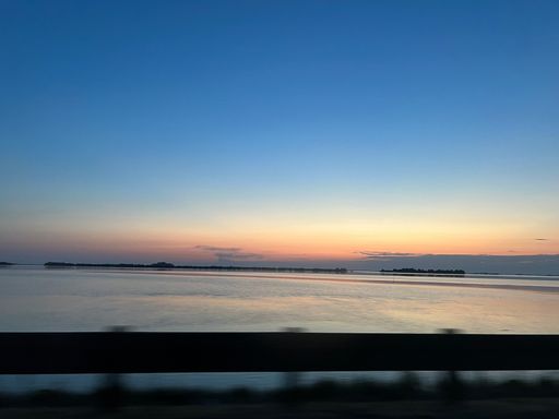 Serene sunset over a calm lake with silhouetted islands and a vibrant sky gradient.