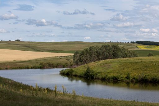 A flowing river surrounded by grassy hills gleaming under the cloudy blue sky