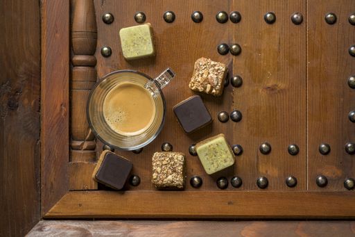 An overhead shot of different types of square-shaped sweets with tea on a wooden tray
