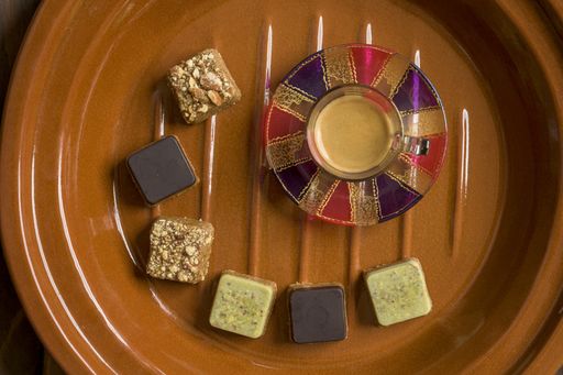 An overhead shot of different types of square-shaped sweets with tea on a wooden tray