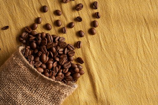 A top view of coffee beans in a burlap bag scattered on a tablecloth