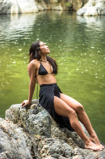 A vertical shot of a Hispanic woman in a swimsuit posing near the lake