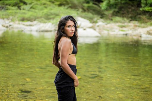 A scenic view of a Hispanic woman in a swimsuit posing near the lake