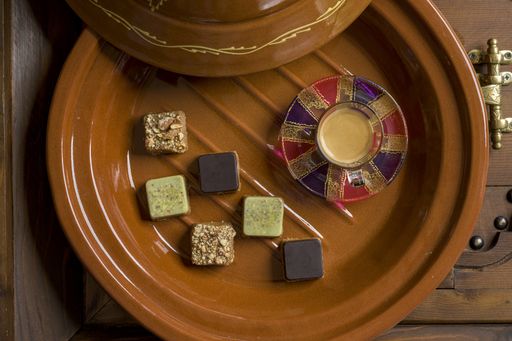 An overhead shot of different types of square-shaped sweets with tea on a wooden tray