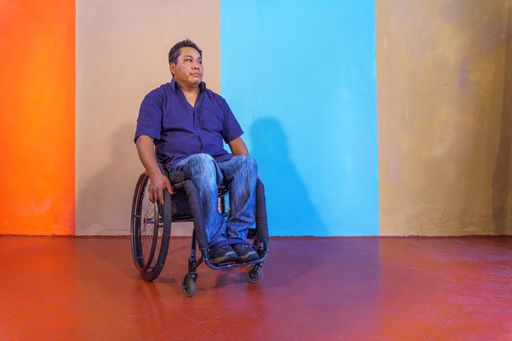 A middle-aged Hispanic man with disabilities on a wheelchair against a colorful background