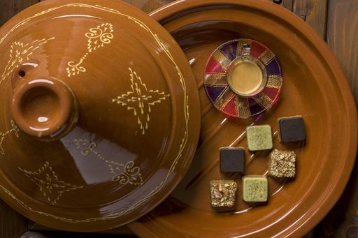 An overhead shot of different types of square-shaped sweets with tea on a wooden tray