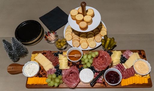 A gourmet charcuterie board with assorted cheeses, meats, grapes, and crackers on a wooden tray, perfect for a festive gathering.