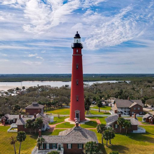 Aerial view of the historic Ponce Inlet Lighthouse with surrounding buildings under a partly cloudy sky in Florida.
