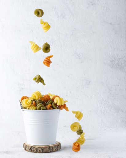 A vertical shot of colorful curly pasta falling in a white tin can