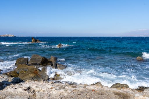 A serene coastal scene with rocky shoreline and blue ocean under a clear sky, ideal for nature and travel themes.