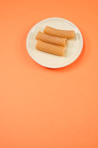 A vertical top view shot of rigatoni on a little white plate on an orange surface with free space for text