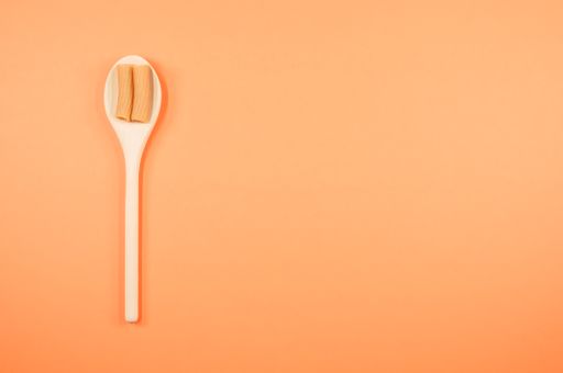 A top view shot of rigatoni on a spoon on an orange surface with free space for text