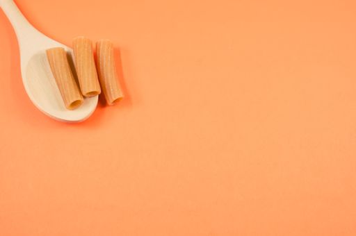 A top view shot of rigatoni on a spoon on an orange surface with free space for text