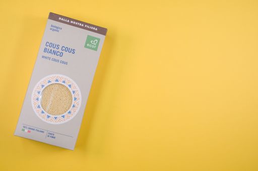 A top view shot of natural organic white Cous Cous in a paperboard package on a yellow surface with free space for text