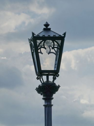 A vertical shot of an old-fashioned street lamp on a post against cloudy sky