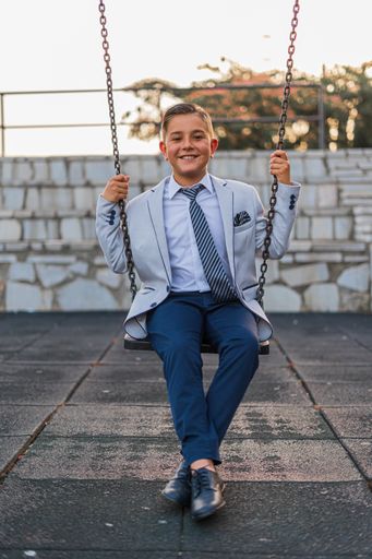 A vertical shot of an adorable male child in a formal suit outfit posing on a swing