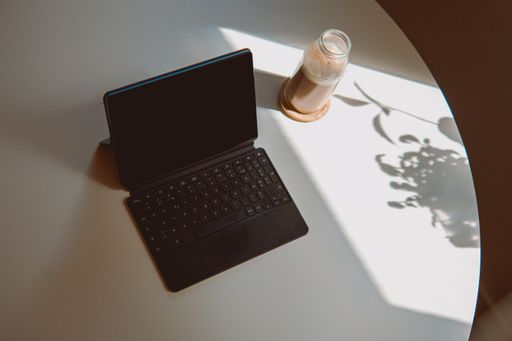 A high angle shot of a bottle of coffee placed on a white desk next to a tablet with a keyboard