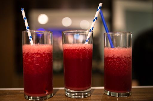 A close-up shot of red foamy cocktails with plastic straws on a wooden bar table