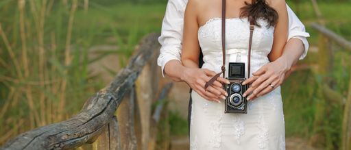 Banner view of an vintage camera in the hands of a newlywed couple taking a picture together.